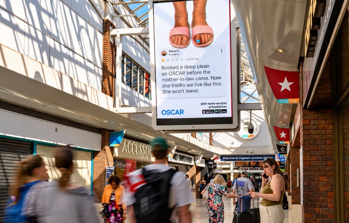OSCAR digital panel at Clapham Junction station in London, showing a one star review from Reena G. and the strapline '200+ home services at fixed prices'
