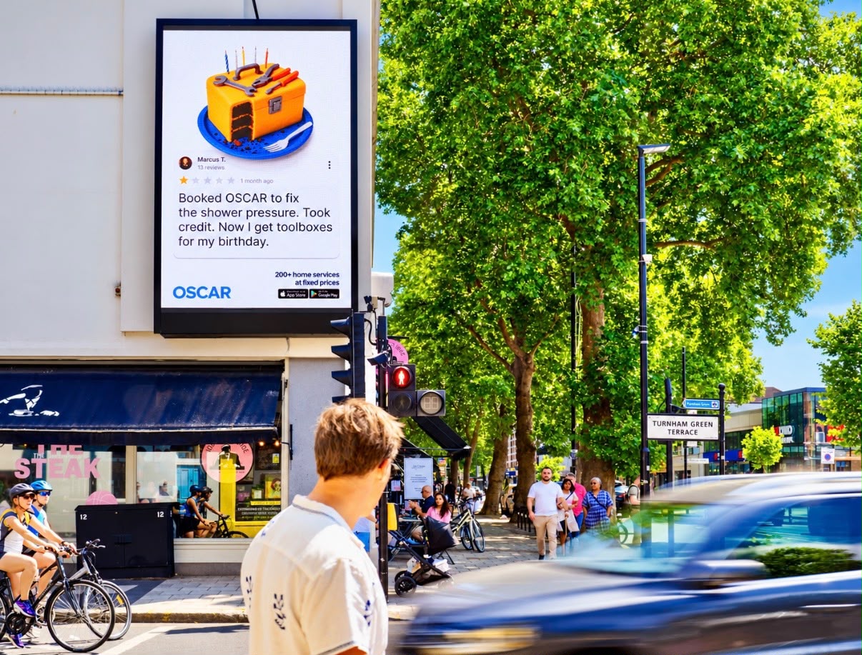 Large format OSCAR digital billboard on Turnham Green Terrace in London showing a one star review from Marcus T. and the strapline '200+ home services at fixed prices'